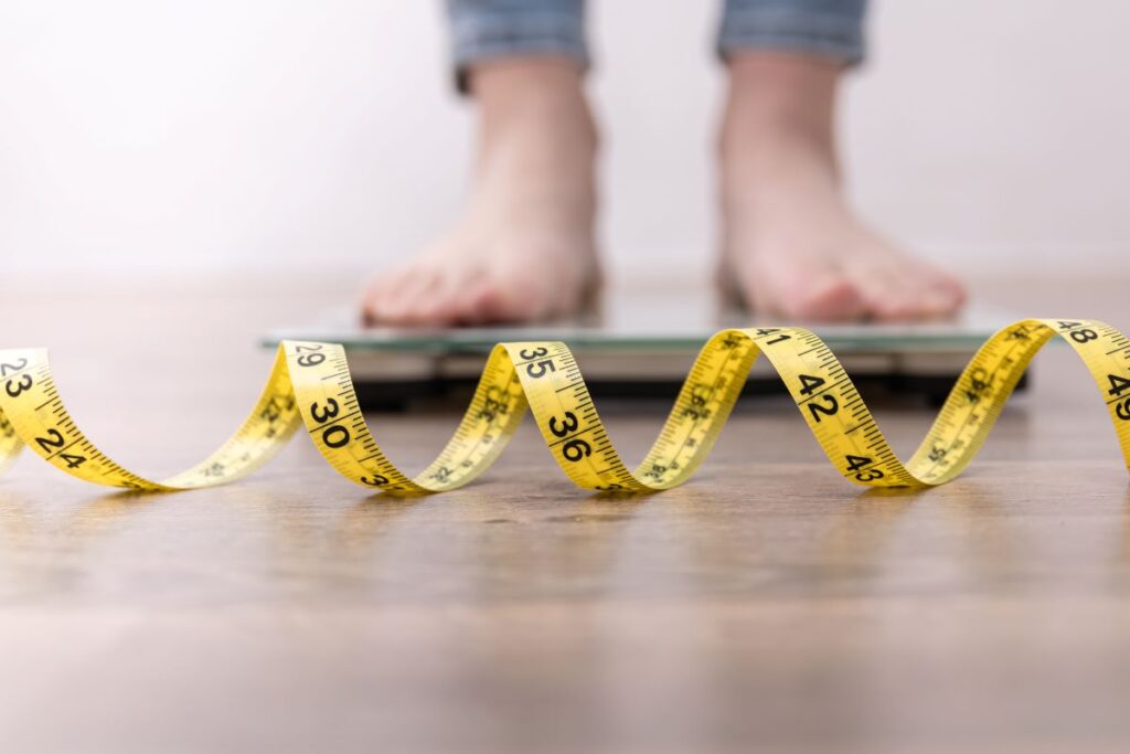 Woman's feet on scales in the background with measuring tape clear in the foreground at the Weight Loss Clinic in Venice, FL